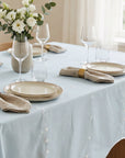 Elegant table setting with light lagoon tablecloth, white flowers, and beige plates.