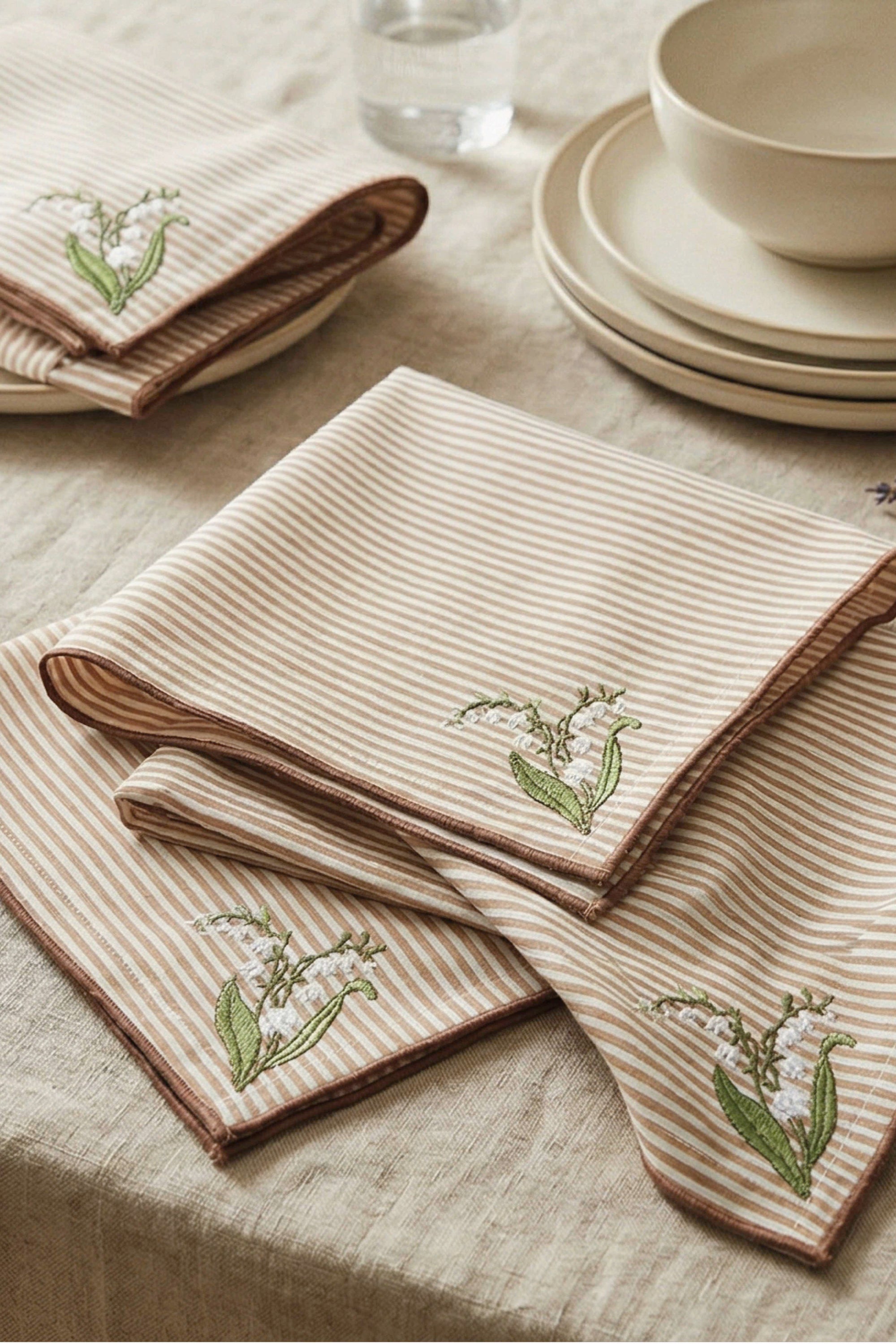Napkins with Lily of the Valley Floral embroidery on a table setting with plates and glasses.