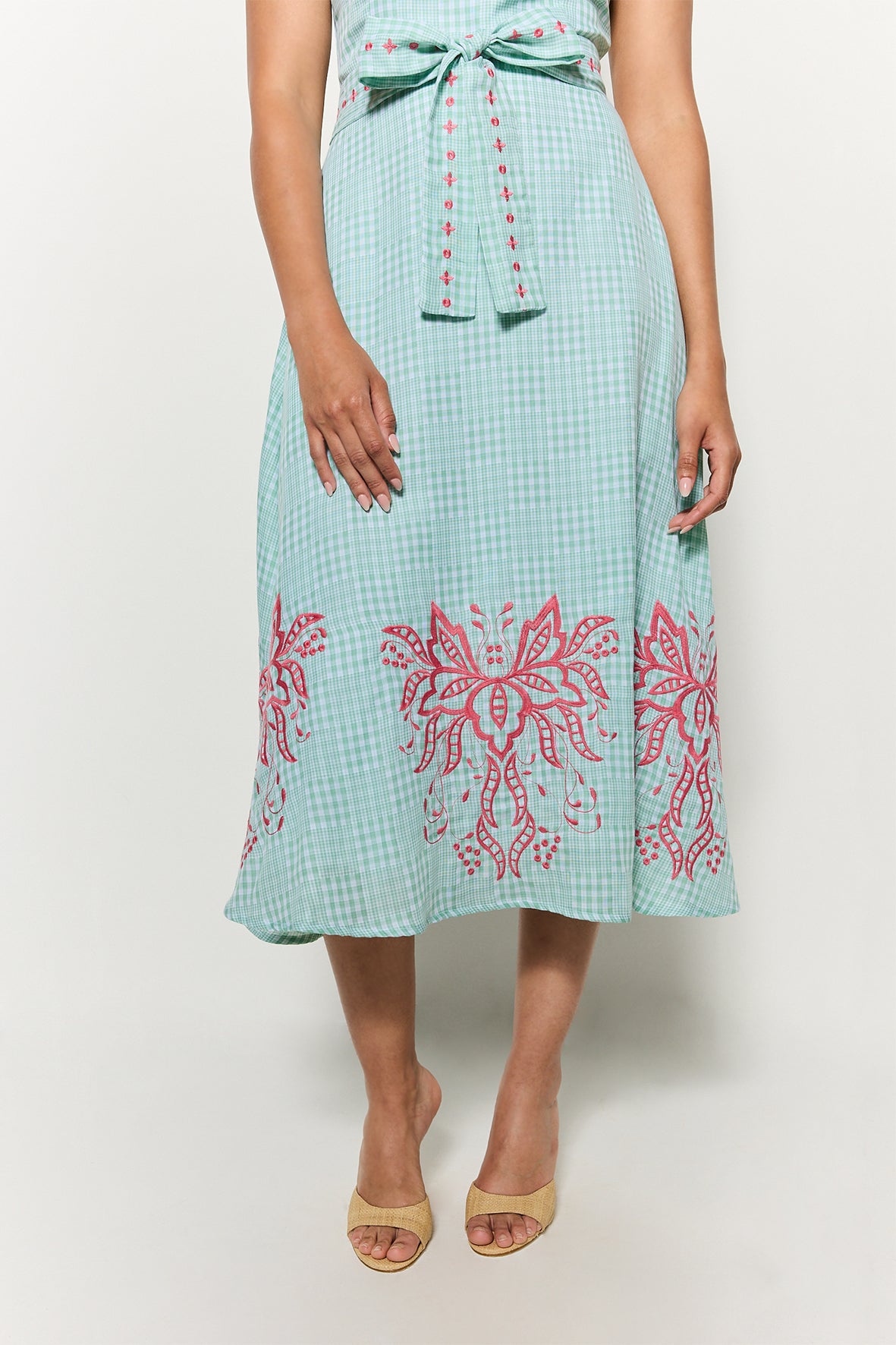Detail shot of Fanm Mon's Libya Midi Dress  showcasing the Green Check plaid print of the babric and the pink floral embroidery on belt and hemline on a white background
