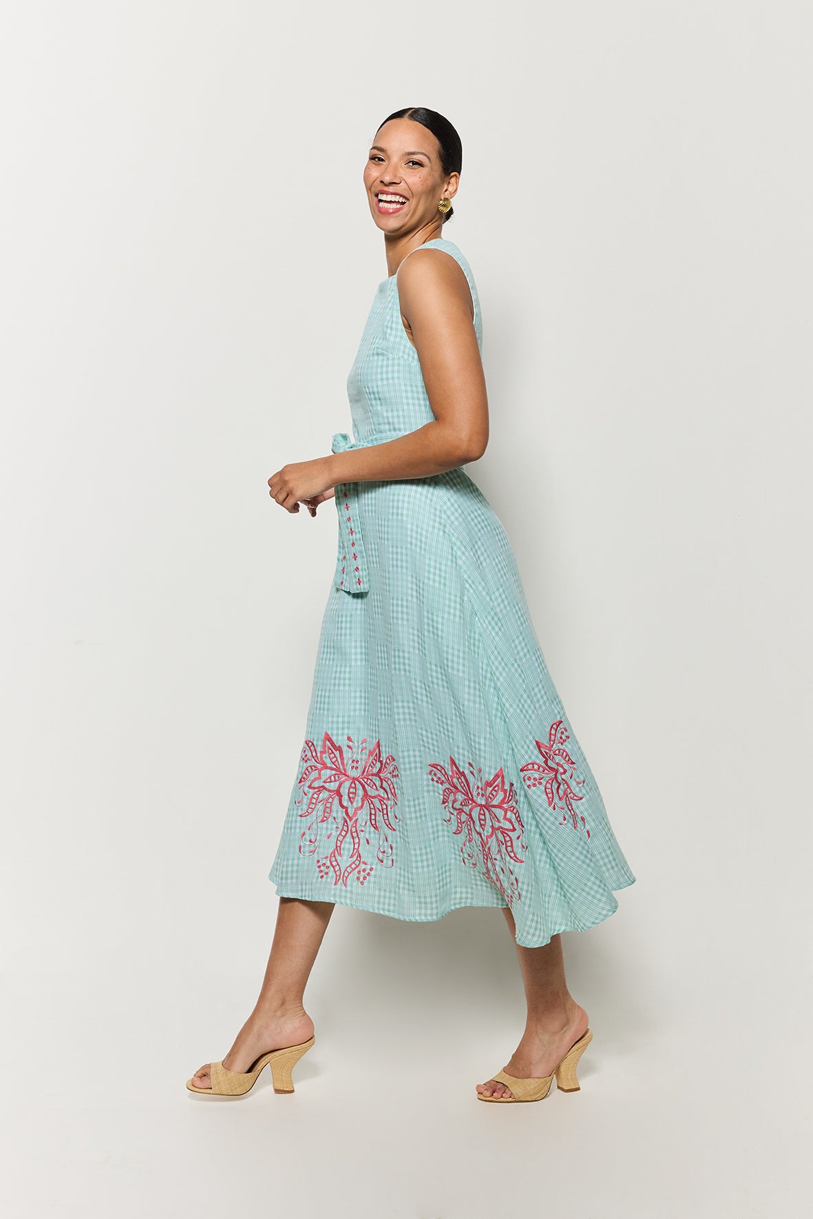 Side view of Model wearing Fanm Mon's Aline Libya Midi Dress in Green Check plaid with pink floral embroidery on a white background.
