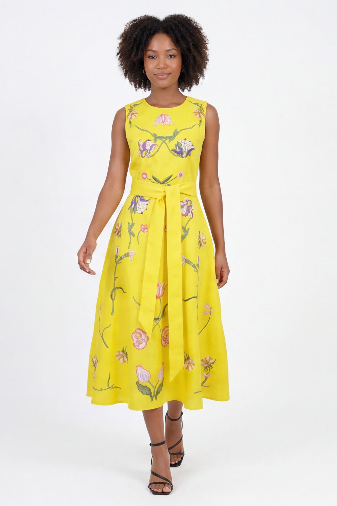 Model wearing the Fanm Mon Nosa Dress featuring tulip-inspired floral embroidery, sleeveless silhouette, self-tie waist belt, and flowing midi skirt in back view against a neutral background.