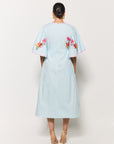 Backview of model in Fanm Mon Tinto Dress in light lagoon with floral embroidery on a white background