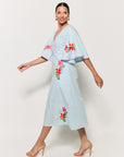 Sideview of Model in Fanm Mon Tinto Dress in light lagoon with floral embroidery showcase flowy ful sleeves and midi length  on a white background