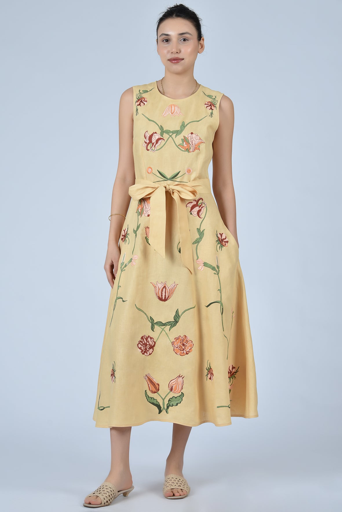 Woman wearing a carmael  dress with floral embroidery on a light gray background