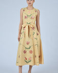 Woman wearing a carmael  dress with floral embroidery on a light gray background