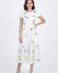 Model wearing the Katrina Dress in white featuring scattered yellow floral embroidery, short sleeves, a belted waist, and a gathered midi hem.