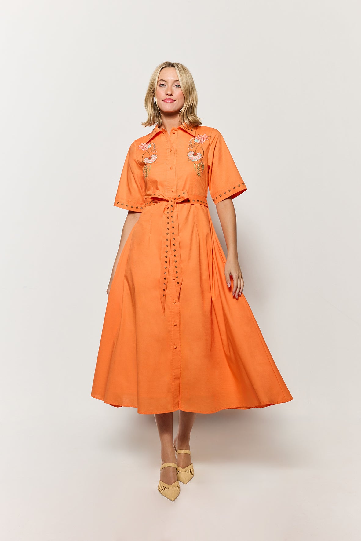 Model Wearing Kenya Midi Length Shirt Dress in Orange, showcasing the movement of the skirt on a white background.