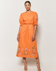 Model Wearing Fanm Mon Pintada Midi Length Dress in Orange with floral embroidery details on white background