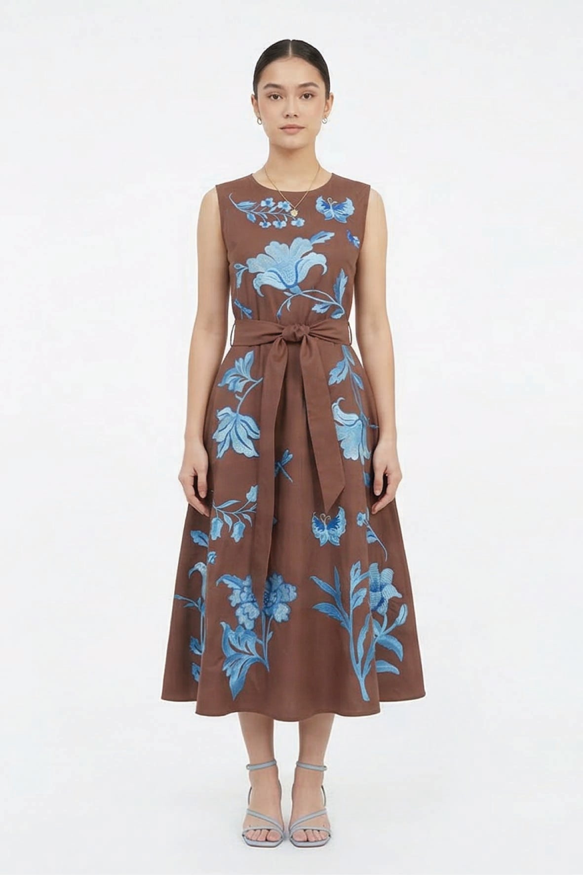 Model wearing the Fanm Mon Gera Dress featuring blue floral embroidery across the bodice and skirt, a round neckline, and self-tie waist belt.