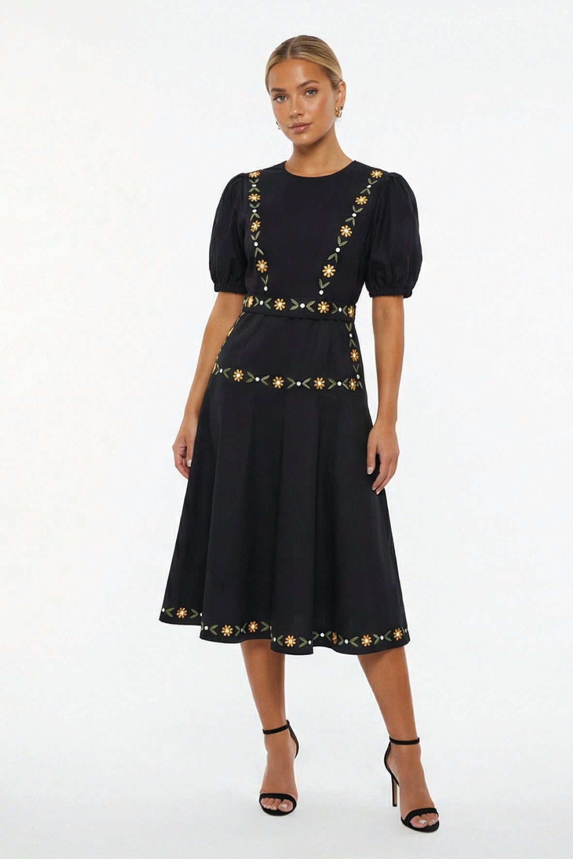 Model wearing the Fanm Mon Lesley Dress featuring a crew neckline, puff short sleeves, hand-embroidered daisy vines, fitted bodice, defined waist, and an A-line midi skirt.