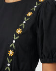 Close-up of the Fanm Mon Lesley Dress highlighting the hand-embroidered daisy vine motif, puff sleeve detailing, and artisan floral embroidery across the bodice.