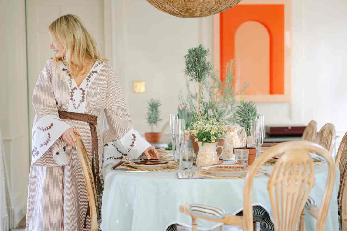 Lauren Neff in a stylish Fanm Mon dress  standing by a dining table with a light blue tablecloth in a room with a fully set table.