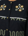 Close-up of the Fanm Mon Pomender Dress highlighting the hand-embroidered daisy blossoms, leafy vine motifs, decorative gold-tone buttons, and artisan embroidery across the bodice.
