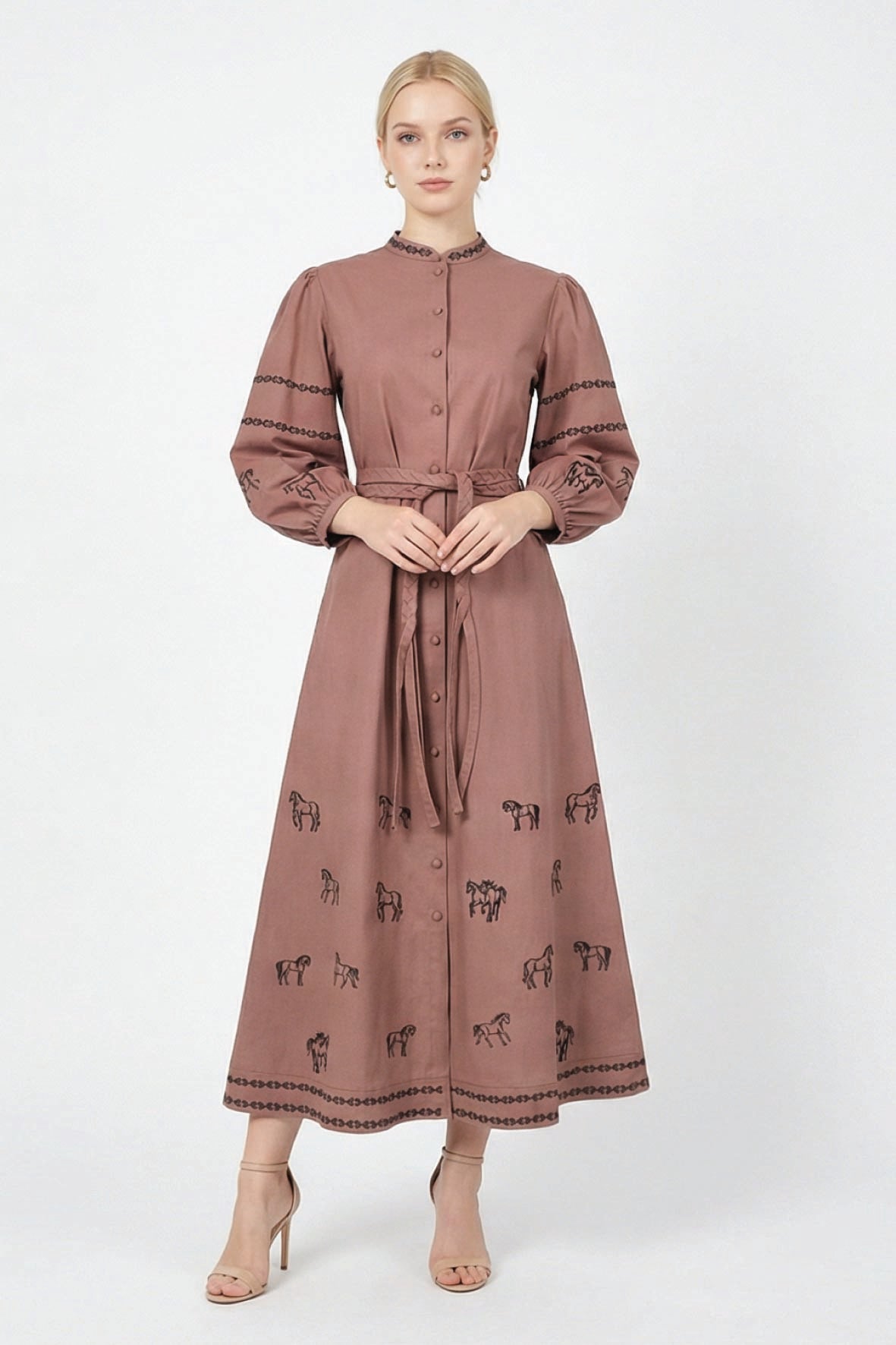 Model wearing the Fanm Mon Sakura Dress featuring black equestrian embroidery, a stand collar, button-front closure, braided self-tie belt, and full midi skirt.
