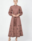 Model wearing the Fanm Mon Sakura Dress featuring black equestrian embroidery, a stand collar, button-front closure, braided self-tie belt, and full midi skirt.