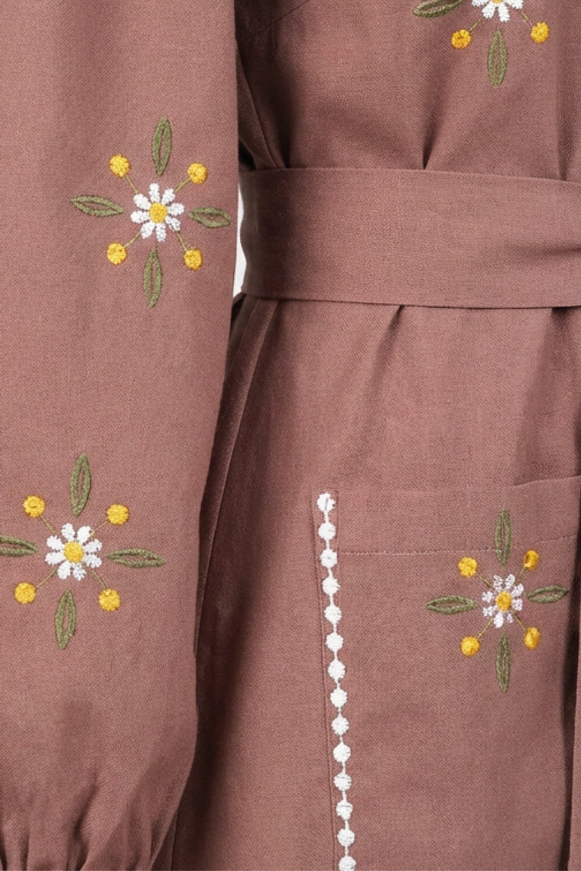 Close-up of the Fanm Mon Samara Dress featuring white and golden-yellow daisy-inspired embroidery, green leaf details, white embroidered trim, and a floral embroidered patch pocket.