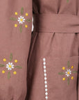 Close-up of the Fanm Mon Samara Dress featuring white and golden-yellow daisy-inspired embroidery, green leaf details, white embroidered trim, and a floral embroidered patch pocket.