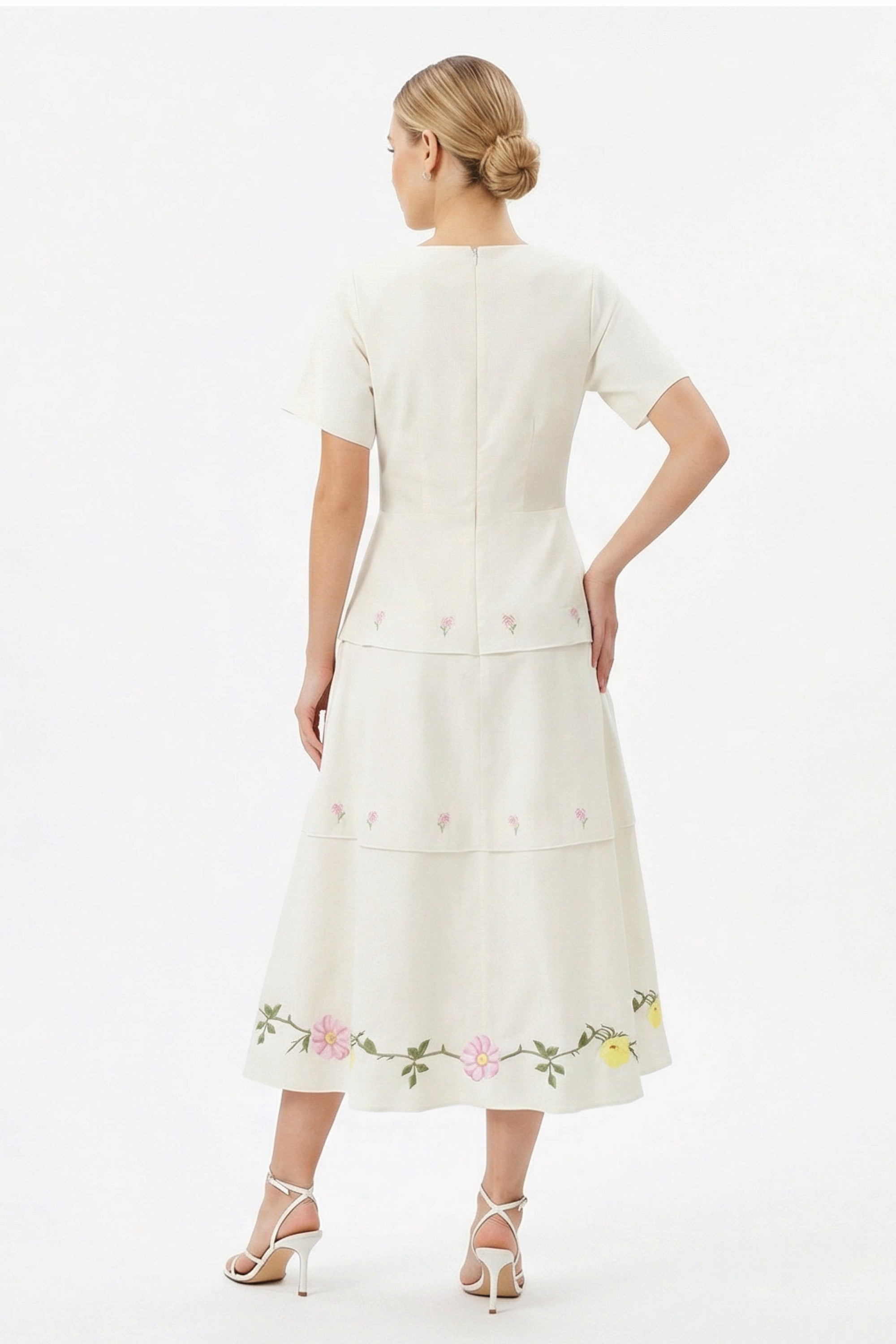Back view of the Fanm Mon Selma Dress showcasing the tailored bodice, concealed back zipper, peplum waist, tiered midi skirt, and embroidered floral border along the hem.