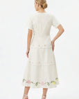 Back view of the Fanm Mon Selma Dress showcasing the tailored bodice, concealed back zipper, peplum waist, tiered midi skirt, and embroidered floral border along the hem.