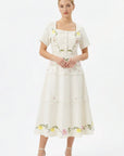 Model wearing the Fanm Mon Selma Dress featuring a square neckline, short sleeves, covered button-front detailing, embroidered bodice, peplum waist, and tiered midi silhouette.