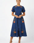 Model wearing the Fanm Mon Simone Dress featuring floral embroidery, short puff sleeves, a self-tie waist belt, and full midi skirt.
