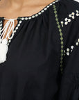 Close-up of a black Stella Dress with white tassel tie, white floral embroidery, and green geometric trim on the neckline and sleeve.