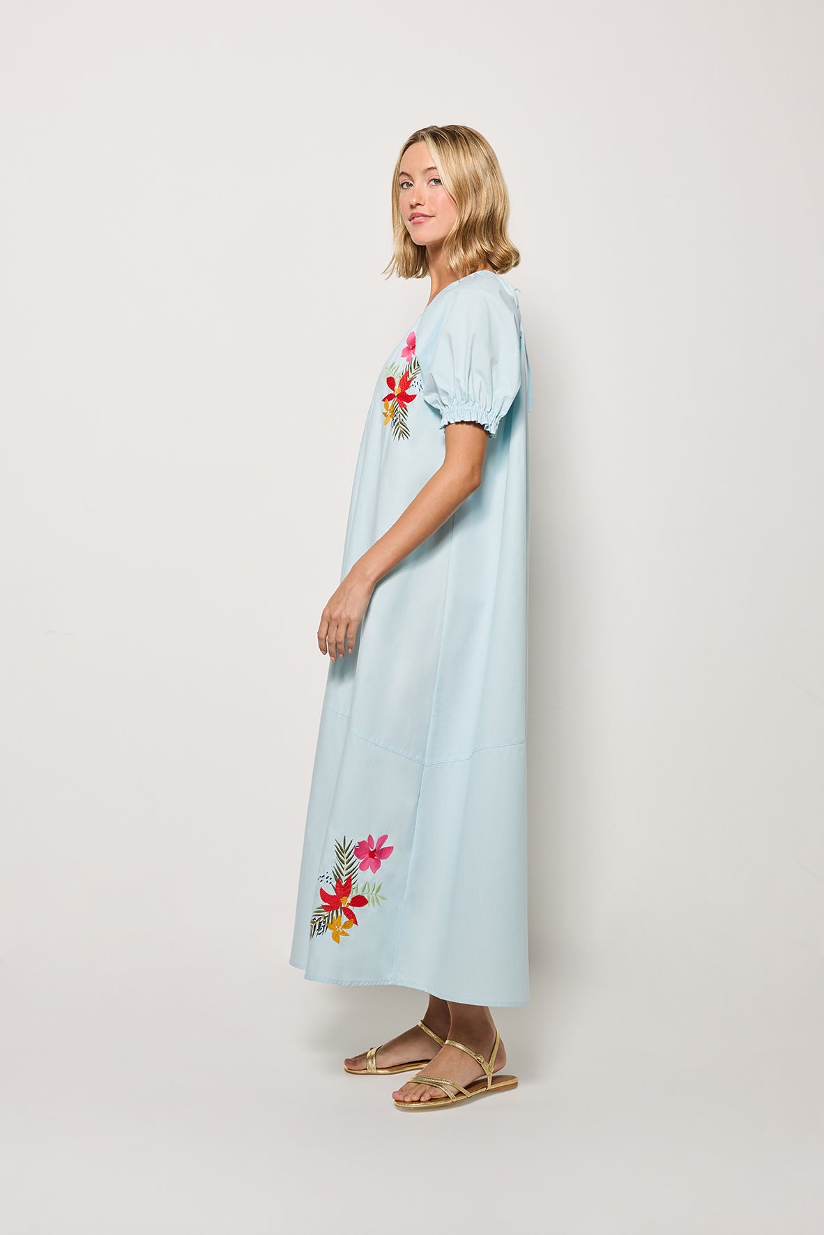 Sideview of Model wearing Fanm Mon's Evora Midi Length dress in Light Lagoon with  floral embroidery on a white background