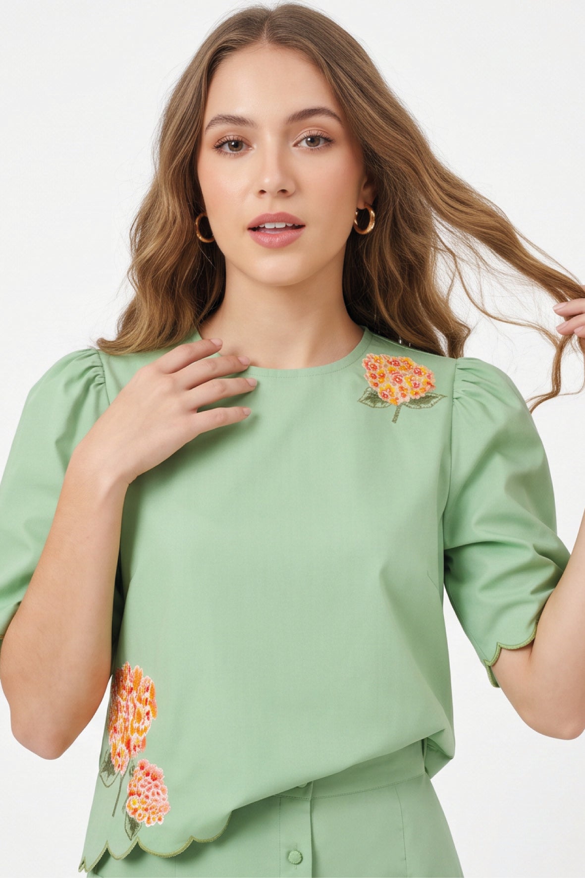 Close-up of Fanm Mon Komarna Set in green highlighting the round neckline, puff sleeves, scalloped hem, and intricate orange, pink, and yellow floral embroidery with green foliage