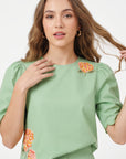 Close-up of Fanm Mon Komarna Set in green highlighting the round neckline, puff sleeves, scalloped hem, and intricate orange, pink, and yellow floral embroidery with green foliage