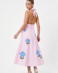 Back view of model wearing the Fanm Mon Ayna Dress with a halter tie, open back and blue floral embroidery.