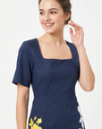 Close-up of the Fanm Mon Blanka Dress in indigo blue highlighting the square neckline, short sleeves, fitted bodice, and yellow rose embroidery at the hip.