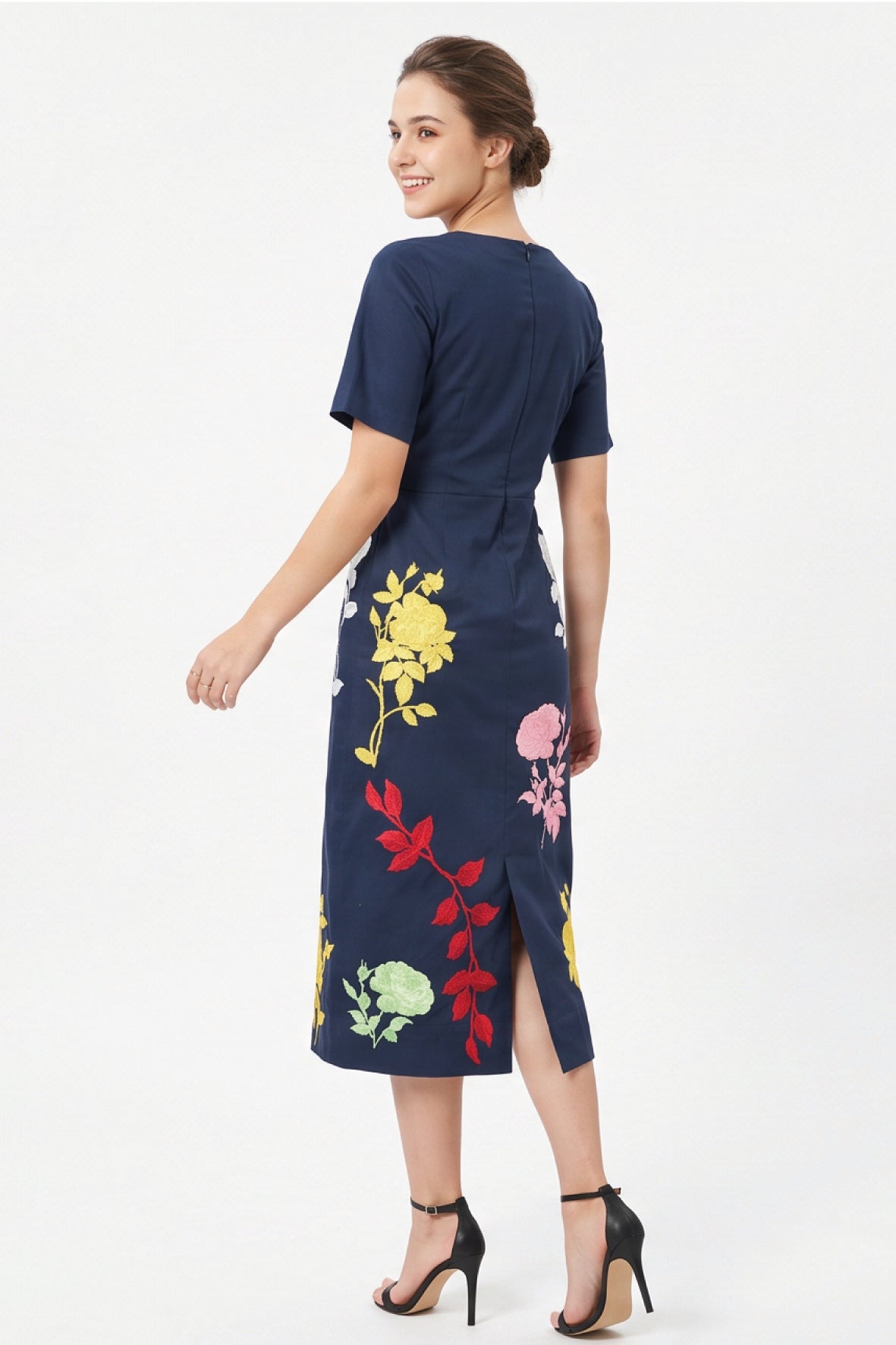 Back view of the Fanm Mon Blanka Dress in indigo blue showing the concealed center-back zipper, back slit, and multicolored floral embroidery extending around the skirt.