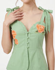 Close-up of Fanm Mon Collette top in green highlighting the scalloped sweetheart neckline, fabric-covered buttons, adjustable shoulder bows, and orange floral embroidery