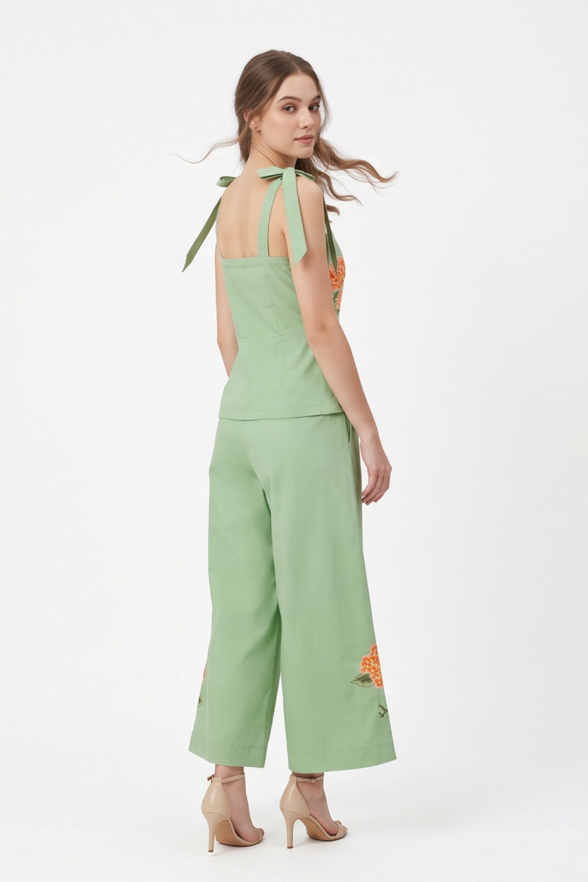 Back view of model wearing Fanm Mon Collette Set in green showing the fitted peplum top, tied shoulder straps, and cropped wide-leg trousers with floral embroidery