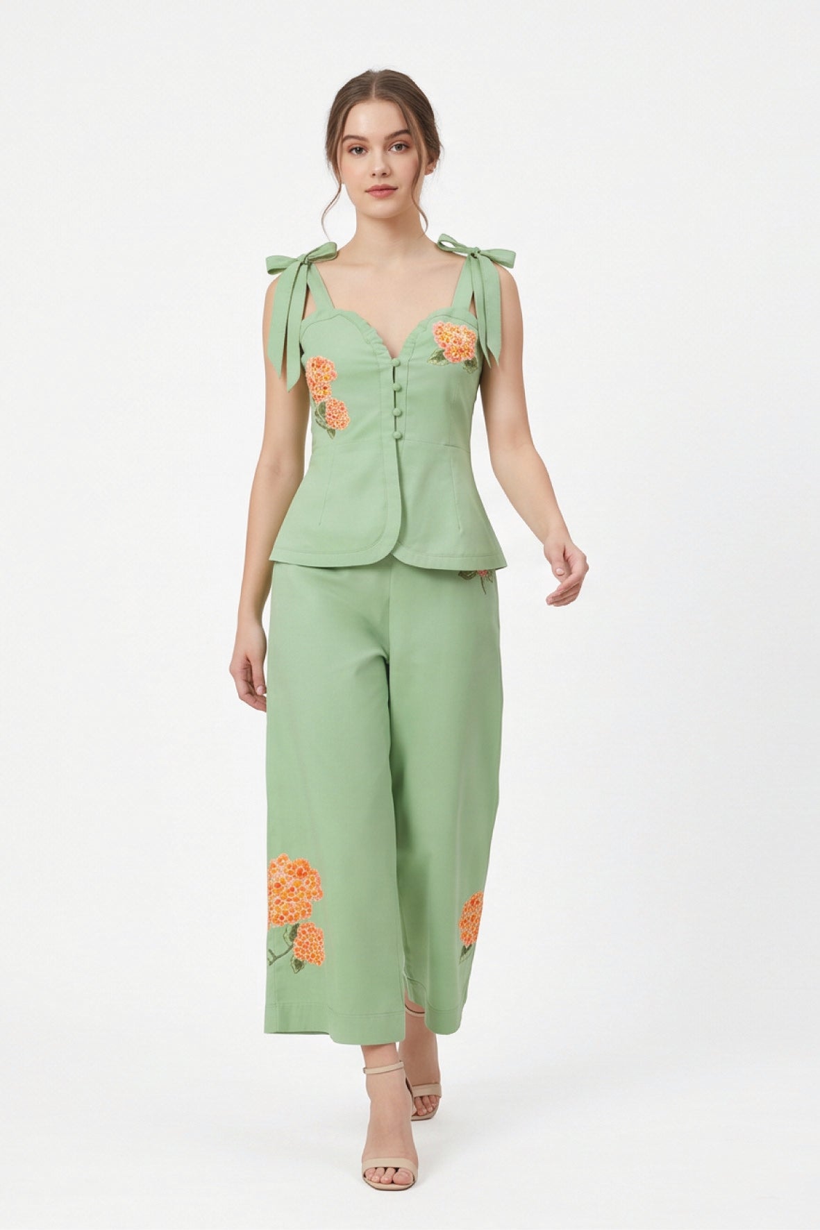 Model wearing Fanm Mon Collette Set in green featuring a structured peplum top with scalloped neckline, shoulder bows, and coordinating floral embroidered cropped trousers