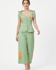 Model wearing Fanm Mon Collette Set in green featuring a structured peplum top with scalloped neckline, shoulder bows, and coordinating floral embroidered cropped trousers