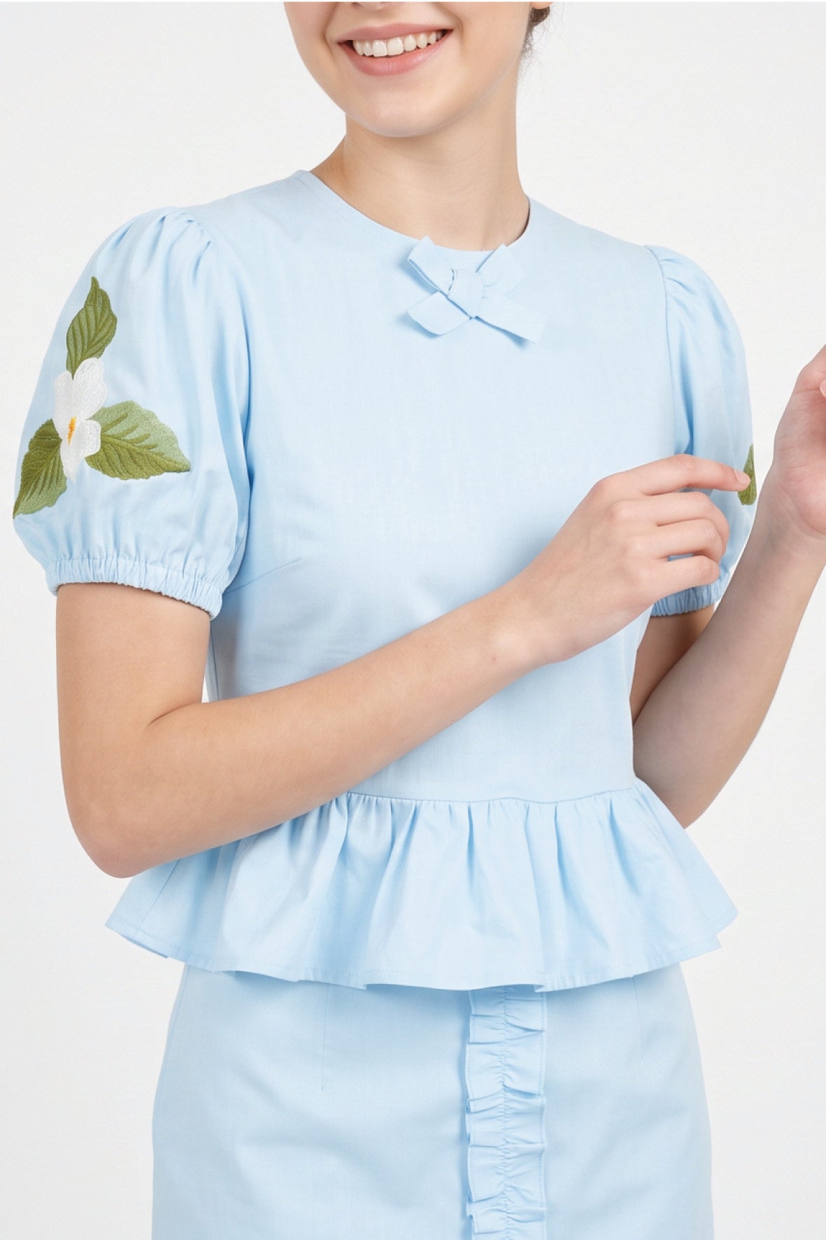 Close-up of Fanm Mon Ether Set in light lagoon highlighting the bow-accented round neckline, puff sleeves, gathered peplum, and white floral embroidery with green leaves