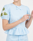 Close-up of Fanm Mon Ether Set in light lagoon highlighting the bow-accented round neckline, puff sleeves, gathered peplum, and white floral embroidery with green leaves