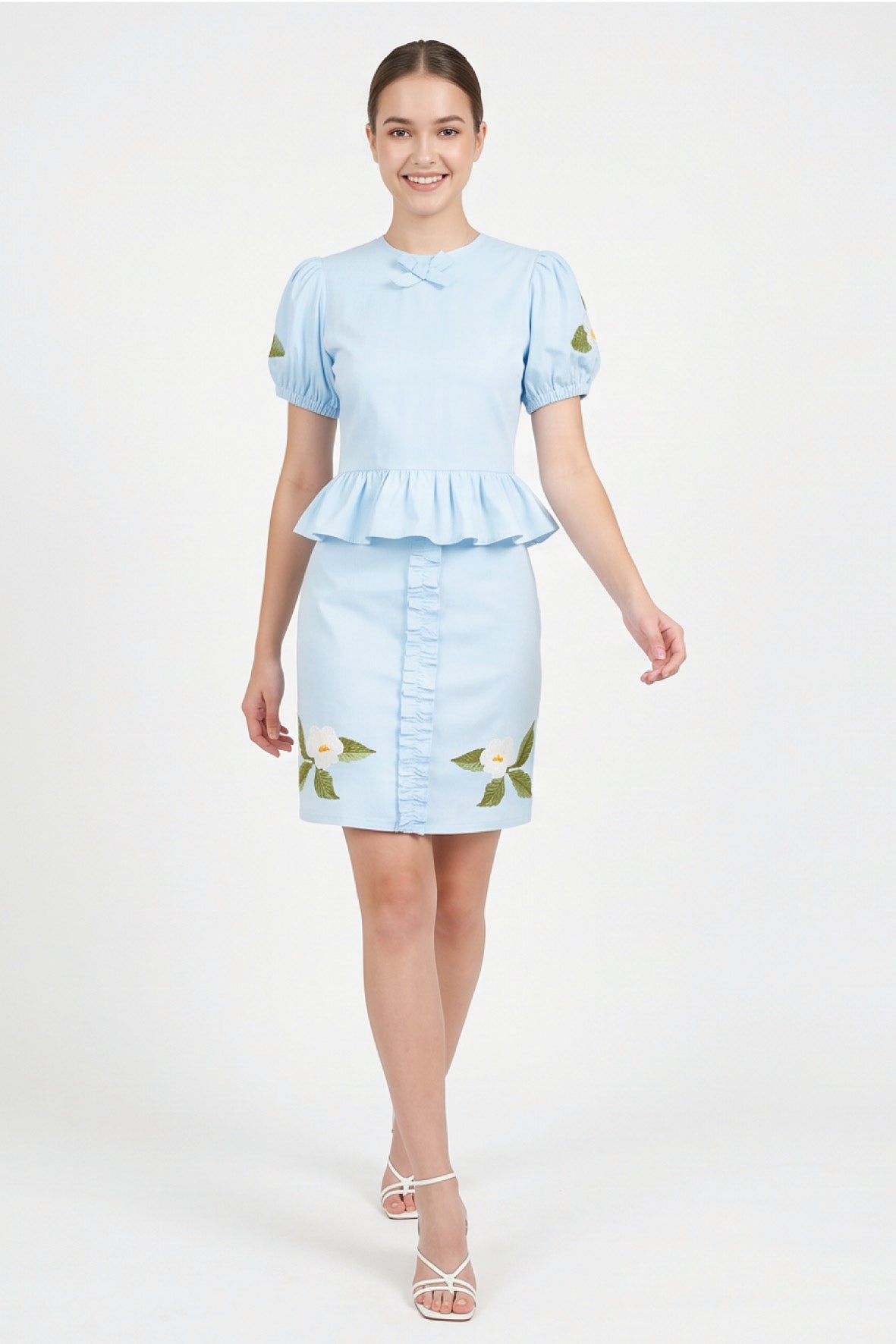 Model wearing Fanm Mon Ether Set in light lagoon featuring a puff-sleeve peplum top, delicate neckline bow, and floral embroidered mini skirt with vertical ruffle detailing