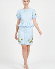 Model wearing Fanm Mon Ether Set in light lagoon featuring a puff-sleeve peplum top, delicate neckline bow, and floral embroidered mini skirt with vertical ruffle detailing