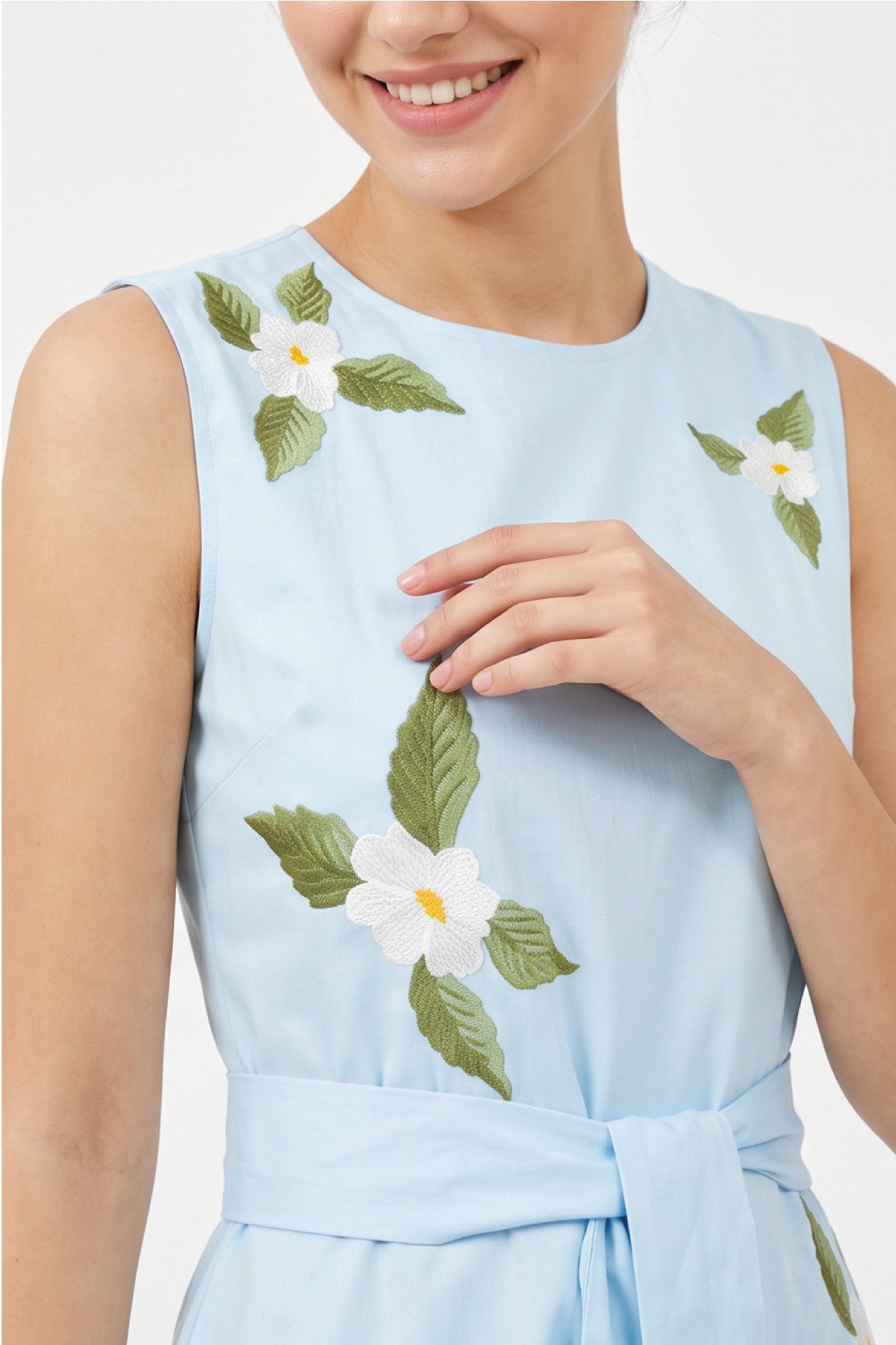Close-up of Fanm Mon Gemimi Dress in light blue highlighting the round neckline, sleeveless bodice, white embroidered flowers with yellow centers, green foliage, and coordinating waist tie.