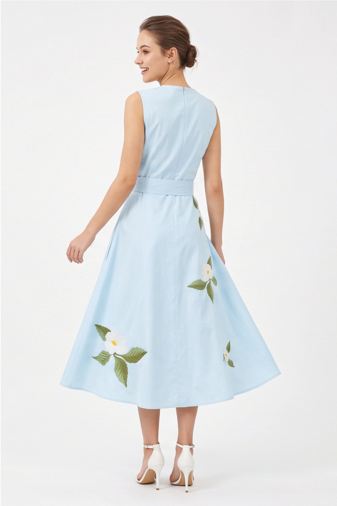 Back view of model wearing Fanm Mon Gemimi Dress in light blue showing the concealed center-back zipper, defined waist, and white floral embroidery along the flowing A-line midi skirt.