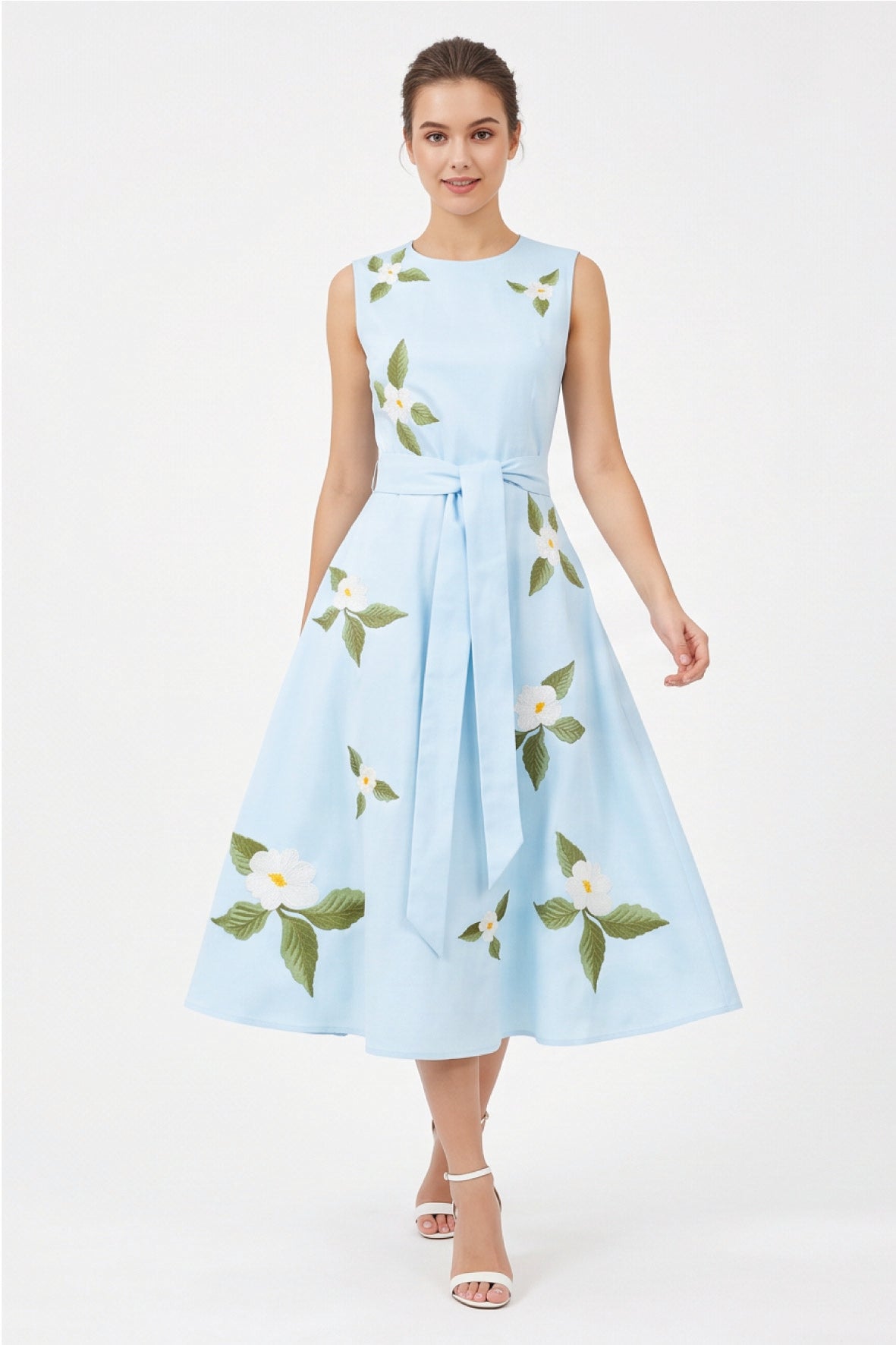 Model wearing Fanm Mon Gemimi Dress in light lagoon with a sleeveless round neckline, self-tie waist belt, and white botanical floral embroidery scattered across the full midi skirt.