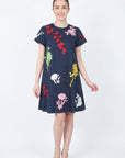 Model wearing the Fanm Mon Gence Dress in navy with a relaxed A-line silhouette and vibrant floral embroidery in pink, red, yellow, green, and white
