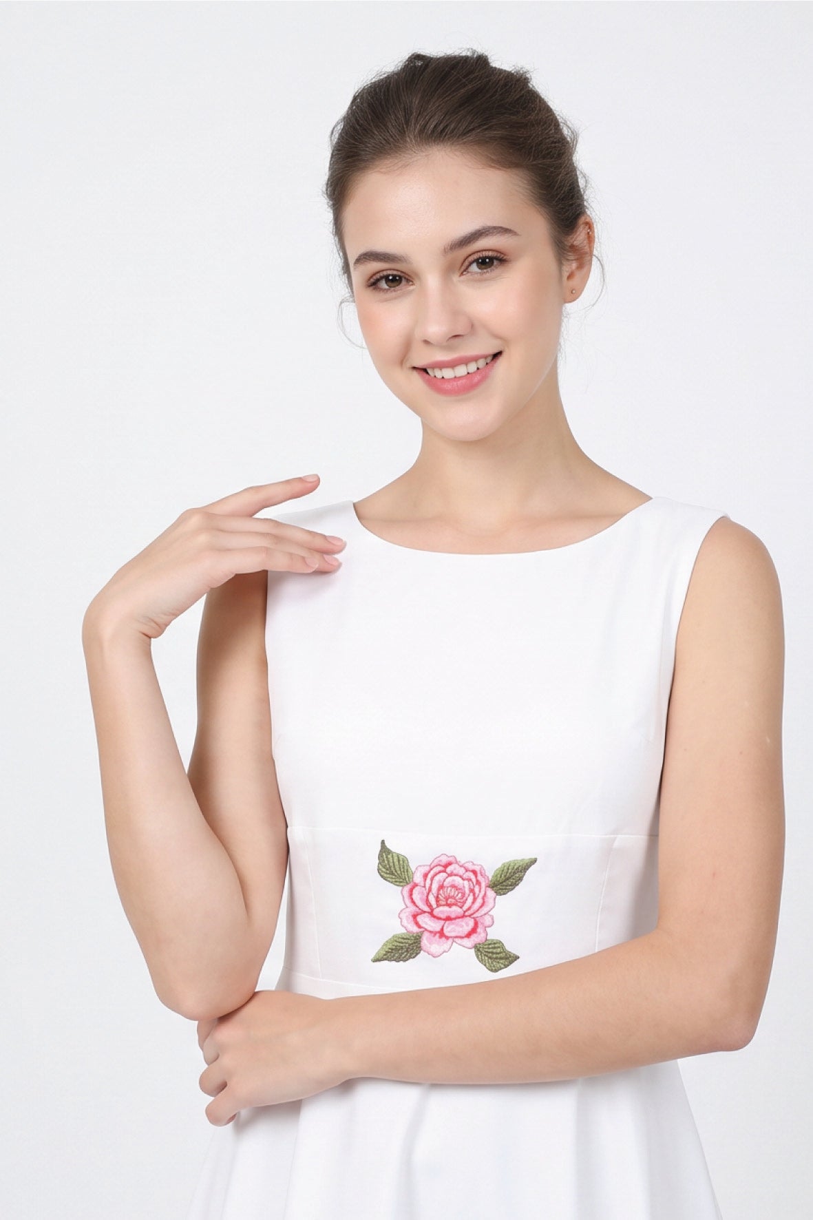 Close-up of model wearing Fanm Mon Hazel Dress in white, highlighting the softly rounded neckline, sleeveless bodice, and central pink rose embroidery with detailed green leaves at the waist.