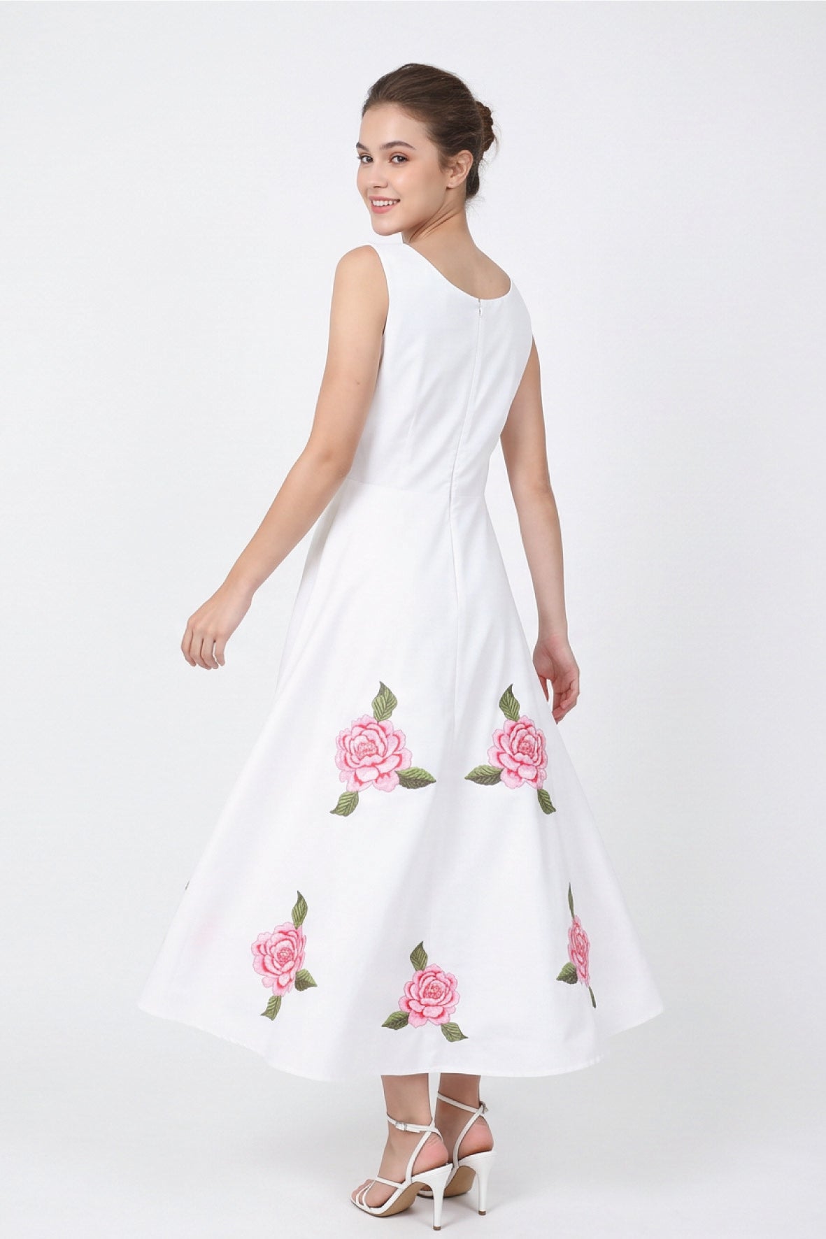 Back view of model wearing Fanm Mon Hazel Dress in white, showing the sleeveless bodice, concealed center-back zipper, defined waist, and pink rose embroidery across the full A-line midi skirt.