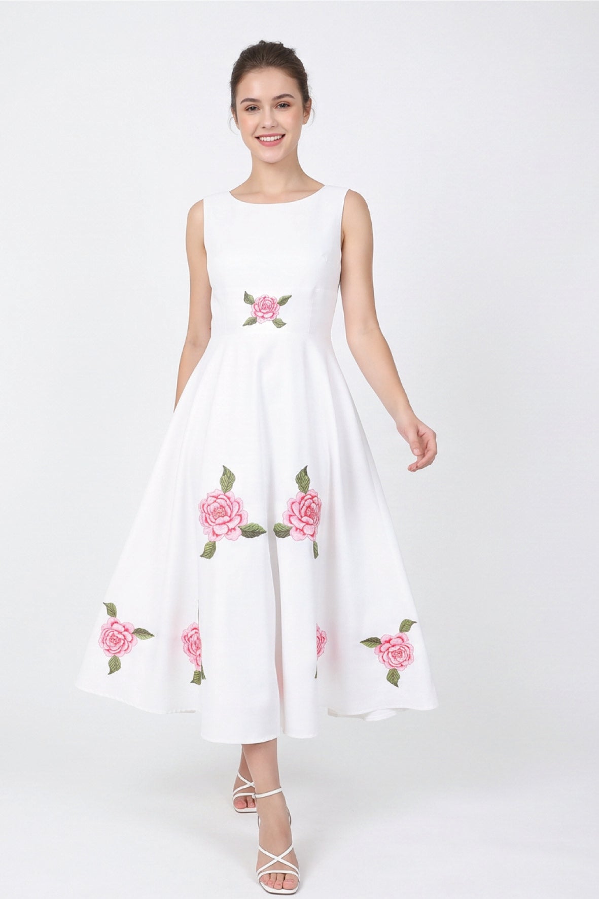 Model wearing Fanm Mon Hazel Dress in white with a round neckline, fitted sleeveless bodice, central pink rose embroidery, and a flowing A-line midi skirt decorated with embroidered roses and green foliage.