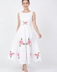 Model wearing Fanm Mon Hazel Dress in white with a round neckline, fitted sleeveless bodice, central pink rose embroidery, and a flowing A-line midi skirt decorated with embroidered roses and green foliage.