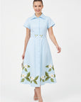 Model wearing Fanm Mon Jahan floral embroidered shirt dress in light blue with a button-front closure, defined waist, and white botanical embroidery along the hem