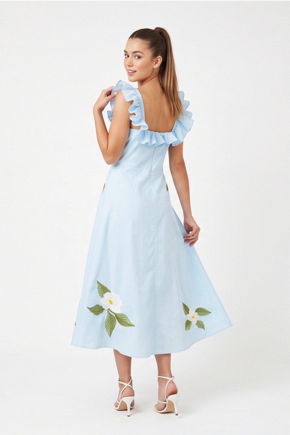 Back view of model wearing Fanm Mon July Dress in light blue with a low square back, ruffled shoulder straps, and floral embroidery along the A-line skirt
